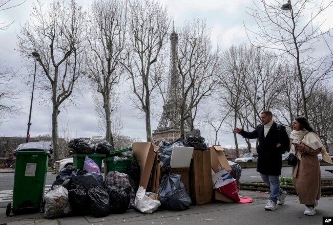 People walk past a pile of garbage near the Eiffel Tower in Paris, March 12, 2023, as strikes continue with uncollected garbage piling higher by the day. (AP Photo/Michel Euler, File)