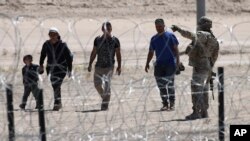 FILE - Migrants wait for U.S. authorities, between a barbed-wire barrier and the border fence at the U.S.-Mexico border, as seen from Ciudad Juarez, Mexico, May 10, 2023.