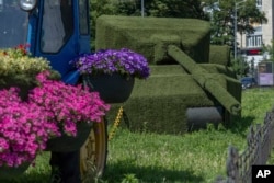 A tractor decorated with flowers is seen linked with a chain to a grass-covered Russian tank, in Kyiv, Ukraine, June 26, 2024.