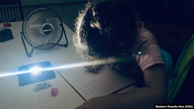 Una niña de 5 años realiza sus tareas escolares durante un apagón en Maracaibo, estado Zulia, en mayo de 2023, mientras usa una lámpara y un ventilador de baterías recargables.