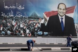 Workers clean the street under a billboard supporting Egyptian President Abdel-Fattah el-Sissi for the presidential elections, in Cairo, Egypt, Dec. 10, 2023.