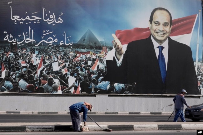 Workers clean the street under a billboard supporting Egyptian President Abdel Fattah el-Sissi for the presidential elections, in Cairo, Egypt, Dec. 10, 2023.