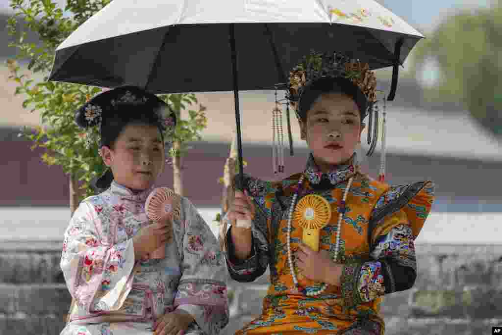 Children dressed in traditional costumes hold an umbrella and cool themselves with portable electric fan outside the Forbidden City on a sweltering day in Beijing.