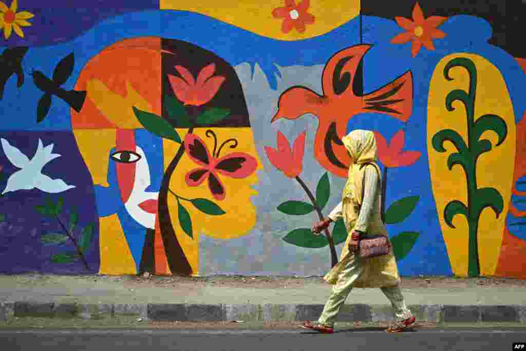 A woman walks past a mural along a a street in New Delhi, India.