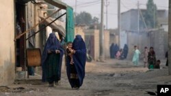 FILE - Burqa-clad Afghan women walk on a street in a neighborhood where mostly Afghan populations live, in Karachi, Pakistan, Jan. 26, 2024. 