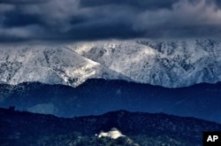 Storm clouds and snow are seen over the San Gabriel mountain range behind Griffith Observatory in the Hollywood Hills part of Los Angeles, Feb. 26, 2023.