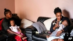Caroline lkendi, right, feeds her twin son Creflo Curtis with baby formula as nanny Hadijja holds her other baby, Roylty Curtis, at lkendi's home in Kampala, Uganda, May 21, 2024.