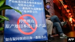 FILE - People are seen at an area of Japanese restaurants where there is a sign reading 'Suspend the sale of all fish products imported from Japan', in Beijing on Aug. 27, 2023. 