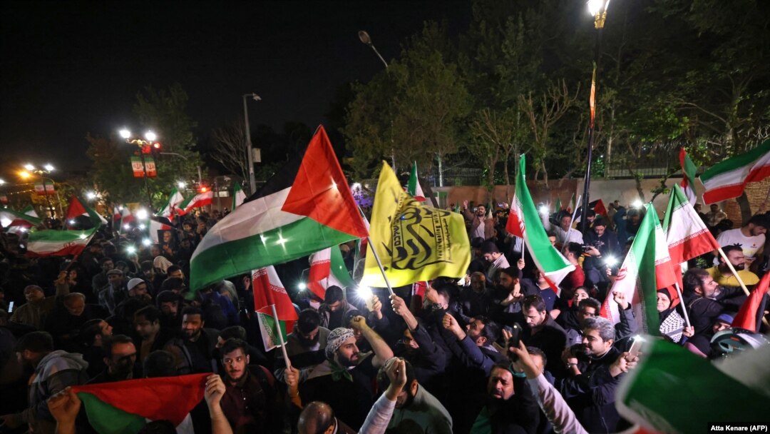 Para demonstran melambaikan bendera Iran dan Palestina saat demo di depan Kedutaan Besar Inggris di Teheran, Minggu, 14 April 2024, setelah Iran meluncurkan serangan drone dan misil ke Israel. (Foto: Atta Kenare/AFP)