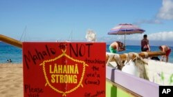 FILE -A man sets up an umbrella in front of a Lahaina Strong informational sign, Dec. 6, 2023, Kaanapali Beach in Lahaina, Hawaii.