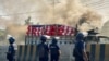 Polisi Bangladesh berdiri di samping truk kargo yang dibakar oleh pekerja garmen di Shafipur, 31 Oktober 2023, dalam aksi protes menuntut upah yang adil. (Munir uz zaman / AFP)