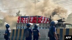 Polisi Bangladesh berdiri di samping truk kargo yang dibakar oleh pekerja garmen di Shafipur, 31 Oktober 2023, dalam aksi protes menuntut upah yang adil. (Munir uz zaman / AFP)