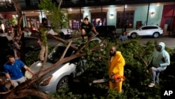 Rapper Trae tha Truth, in yellow, cuts fallen tree limbs on top of a car in the aftermath of a severe thunderstorm that passed through downtown, May 16, 2024, in Houston.