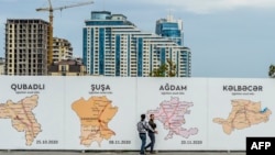 FILE - People walkspast a poster showing the maps of the towns of Nagorno-Karabak in Baku on Sept. 13, 2023. 