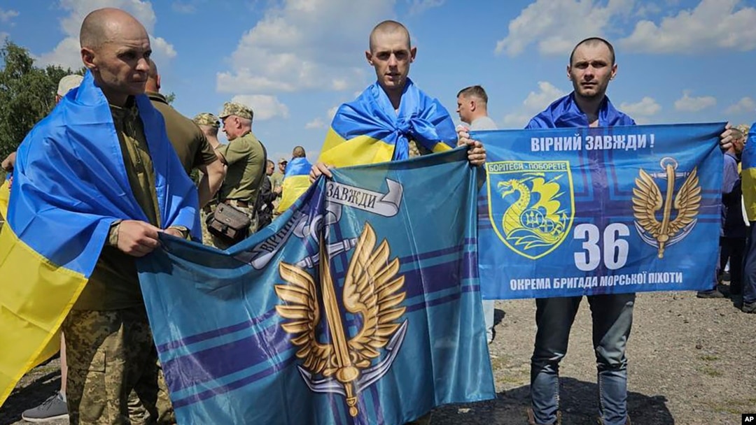 In this photo provided by the Ukrainian Presidential Press Office on July 17, 2024, Ukrainian prisoners of war hold Marine flags as they pose for a photo after a prisoners exchange at an undisclosed location in Ukraine.