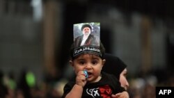 A child carried by a woman wears a picture on his head of Iran's late president Ebrahim Raisi during a rally to mourn the death of the Iranian president and his entourage killed in a recent helicopter accident, in Beirut's southern suburbs.