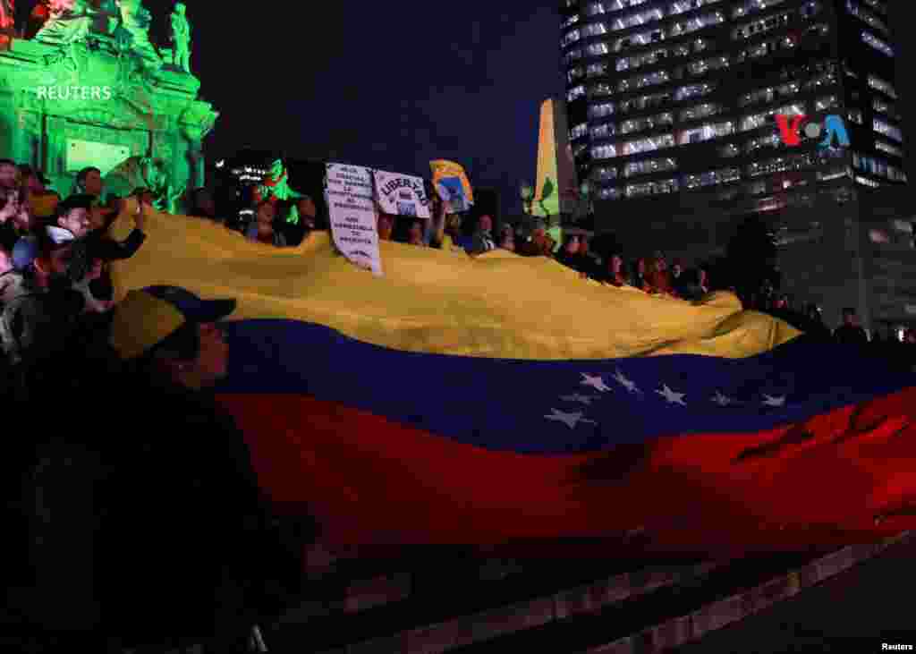 Venezolanos que viven en México y miembros del Comando ConVzla sostienen una bandera venezolana&nbsp;gigante durante una protesta contra los resultados electorales que otorgaron al presidente venezolano Nicolás Maduro un tercer mandato, en el monumento del Ángel de la Independencia en la Ciudad de México.