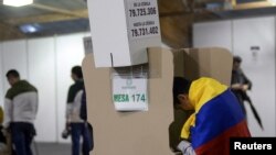 ARCHIVO - Un votante envuelto en la bandera nacional llena una papeleta en una mesa electoral dentro de Corferias durante la segunda vuelta de las elecciones presidenciales en Bogotá, Colombia, el 19 de junio de 2022.