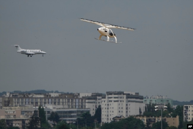 The Volocopter 2X, an electric vertical takeoff and landing multicopter, right, performs a demonstration flight during the Paris Air Show in Le Bourget, north of Paris, France, Monday, June 19, 2023. (AP Photo/Lewis Joly)