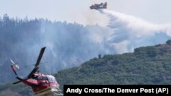 A CL 415 scooper top, drops water on the Quarry Fire as a Firehawk helicopter maneuvers for a water drop southwest of Littleton, Colorado, Aug. 1, 2024. (Andy Cross/The Denver Post via AP)