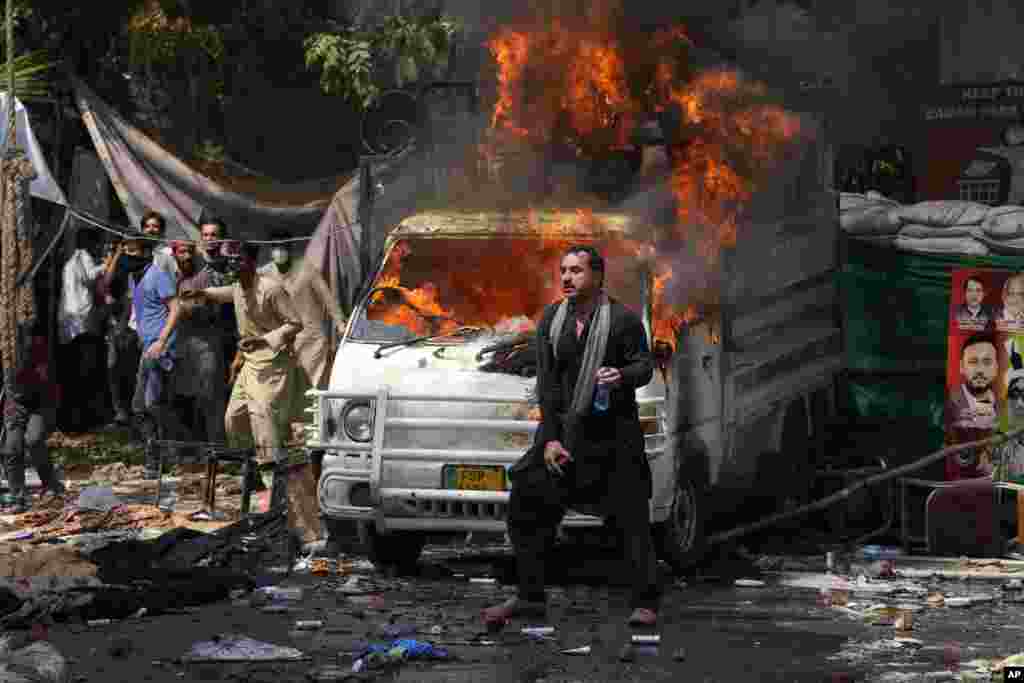 Поддржувачите на поранешниот премиер Имран Кан фрлаат камења кон полицијата додека стојат до запалено возило за време на судирите во Лахоре, Пакистан.
