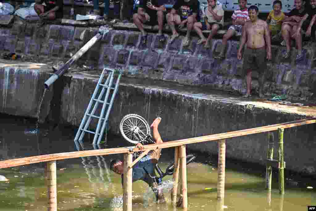 A child falls during a bicycle balance competition over a plank on a river, part of community festivities ahead of the 79th anniversary of Indonesia&#39;s Independence Day, in Surabaya.