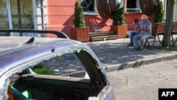 Local residents sit near a damaged car at the site of a missile strike in Chernihiv, Aug.19, 2023.