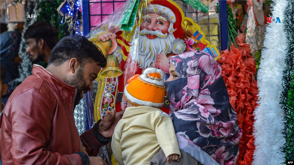 Desde Pakistán: Una familia junto a una tienda que vende adornos navideños en Karachi el 23 de diciembre de 2023.