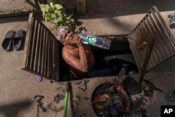 FILE - A man drinks water as he takes a break from cleaning underground sewage on a hot day in Mumbai, India, May 2, 2024.