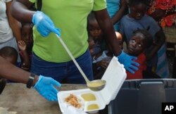 A server ladles soup into a container as children line up to receive food at a shelter for families displaced by gang violence, in Port-au-Prince, Haiti, March 14, 2024.