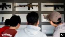 ARCHIVO - Varias personas miran los fusiles en una pared de exhibición en una tienda en Auburn, EEUU.