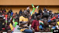 A man waves Niger, Mali and Burkina Faso flags as supporters cheer from the stands while artists perform during a concert in support to Niger's National Council for the Safeguard of the Homeland at General Seyni Kountche Stadium in Niamey, Aug. 13, 2023. 