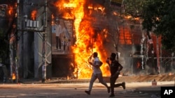 Men run past a shopping center which was set on fire by protesters during a rally against Prime Minister Sheikh Hasina and her government, in Dhaka, Bangladesh, Aug. 4, 2024. 