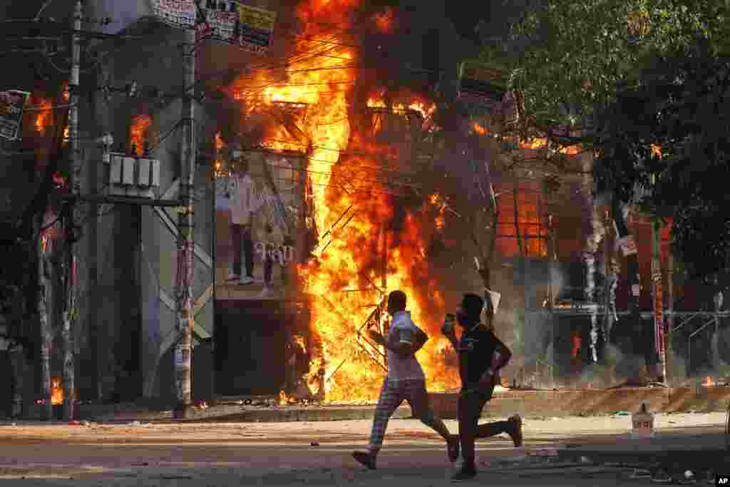 Men run past a shopping center which was set on fire by protesters during a rally against Prime Minister Sheikh Hasina and her government demanding justice for the victims killed in the recent countrywide deadly clashes, in Dhaka, Bangladesh.