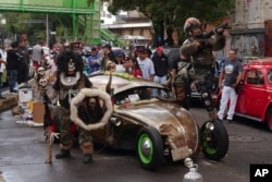 People dressed as skeletons and combat fighters pose for a photo next to their antique Volkswagen Beetle, known in Mexico as "vocho," before a parade the day after World Vocho Day, in Mexico City, June 23, 2024.
