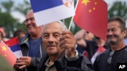 Човек вее кинески и српски знамиња додека го чека доаѓањето на кинескиот претседател Шји Џинпинг и неговиот српски колега Александар Вучиќ пред Палатата Србија во Белград, 8 мај 2024 година.