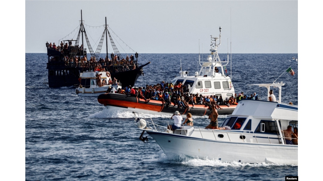 An Italian Coast Guard vessel carrying migrants rescued at sea passes between tourist boats, on Sicilian island of Lampedusa, Sept. 18, 2023.