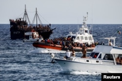 An Italian Coast Guard vessel carrying migrants rescued at sea passes between tourist boats, on Sicilian island of Lampedusa, Sept. 18, 2023.