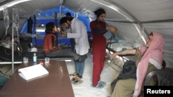 A health worker examines a boy affected by the earthquake inside a mobile clinic in rebel-held town of Jandaris, Syria, Feb. 14, 2023.