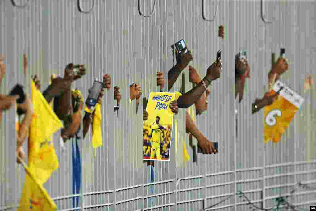 Fans carry a poster of Chennai Super Kings&#39; MS Dhoni and take pictures through a fence as they wait for the Indian Premier League cricket match between Chennai Super Kings and Punjab Kings to begin in Chennai.