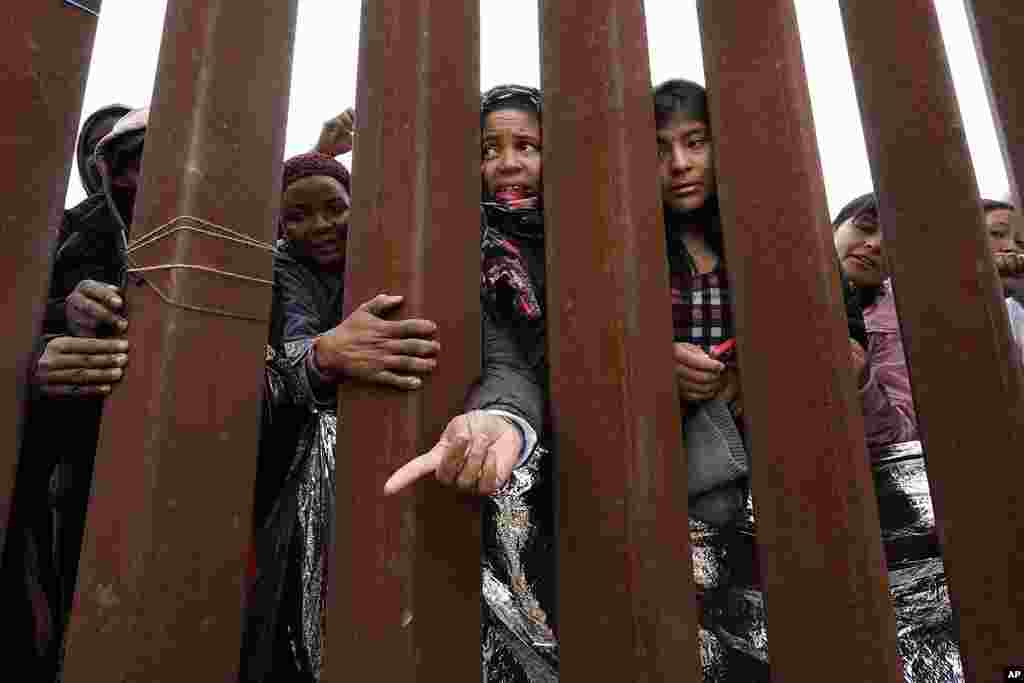 Migrants reach through a border wall for clothing handed out by volunteers, as they wait between two border walls to apply for asylum, in San Diego, California. Hundreds of migrants remain waiting between the two walls.