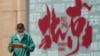 A boy browses a tablet computer as he walks by a billboard promoting tourism destination outside a shopping mall in Beijing, July 19, 2023. 