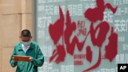 A boy browses a tablet computer as he walks by a billboard promoting tourism destination outside a shopping mall in Beijing, July 19, 2023. 