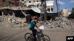 Seorang anak laki-laki Palestina menaiki sepeda melewati gedung-gedung yang hancur di Rafah, di selatan Jalur Gaza, pada 26 Mei 2024. (Foto: AFP/Eyad Baba)