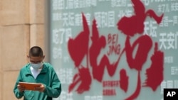 FILE - A boy browses a tablet computer as he walks by a billboard promoting tourism destinations in Beijing on July 19, 2023. China fully reopened to tourists in March, but some statistics show foreign visitors are staying away.