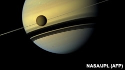 Снимок Титана, сделанный зондом «Кассини». На заднем плане – планета Сатурн.