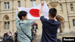 People hold up a Japanese flag as they gather for the visit of Japan's Emperor Naruhito and Empress Masako outside Balliol College at Oxford University, in Oxford, Britain, June 28, 2024.