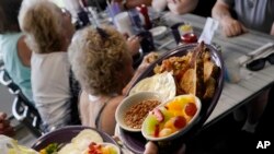 A server carries out a breakfast order for senior citizens participating in the Meals on Wheels "Dine Out Club," at the White Birch Cafe in Goffstown, New Hampshire, July 19, 2023.