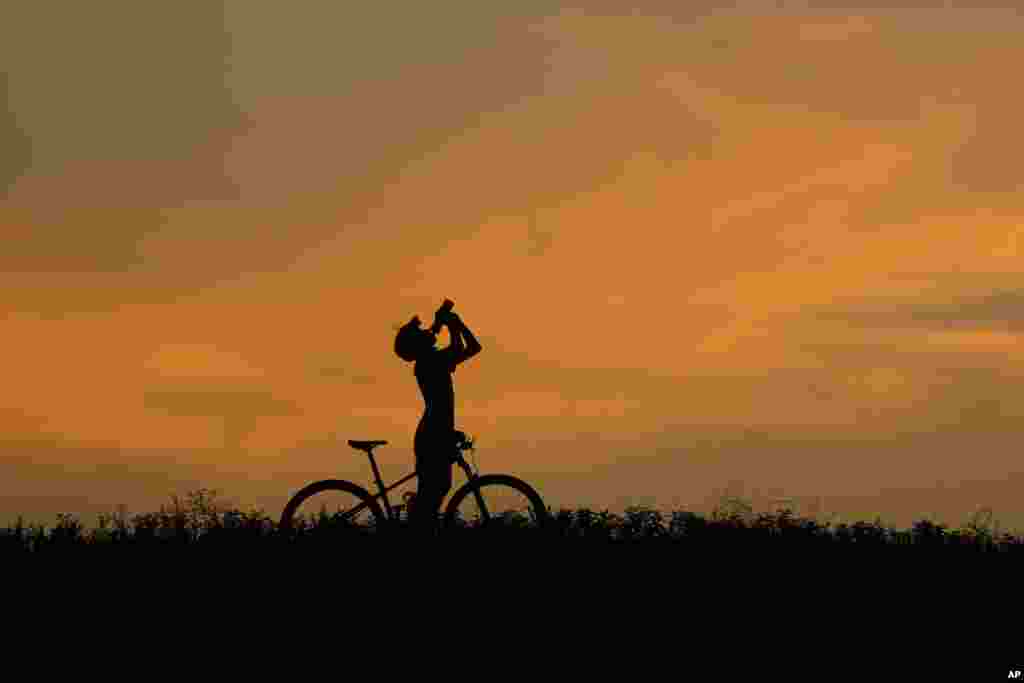 A cyclist takes a water break at dusk in San Antonio, July 1, 2024. South Texas began the month of July with triple digit temperatures. 
