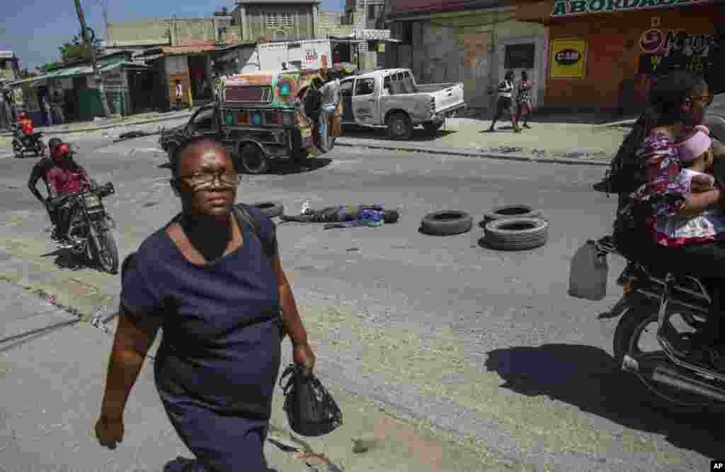 Personas y motociclistas pasan cerca de un hombre asesinado a tiros y cuyo cadáver que quedó tirado a media calle en Puerto Príncipe, Haití, el jueves 20 de abril de 2023. Foto - Odelyn Joseph.